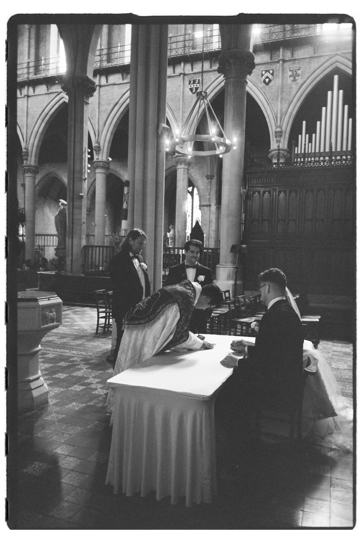 Black and white photo of people gathered around a table inside a grand cathedral with arched columns and organ pipes.