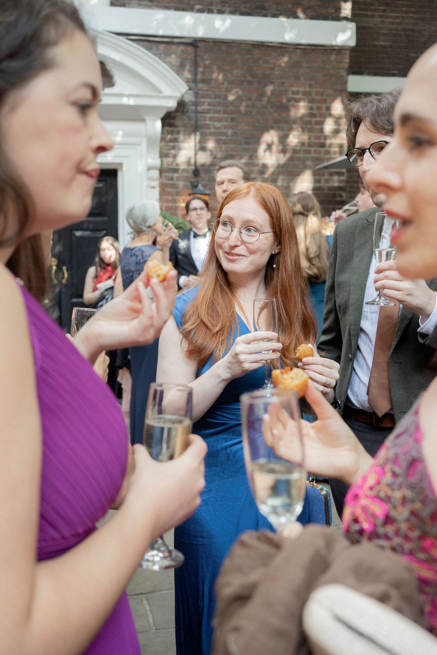 Guests in formal attire socializing outdoors at an elegant event, holding champagne glasses and appetizers.