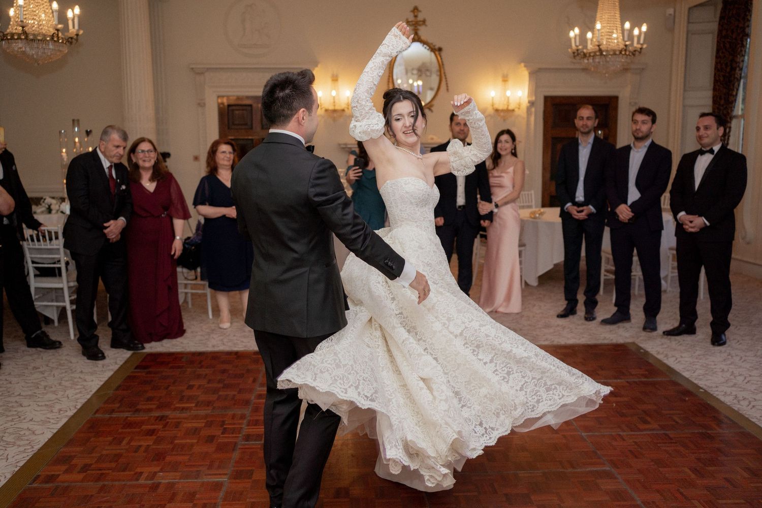 Couple dancing in elegant ballroom with guests watching from the sides.