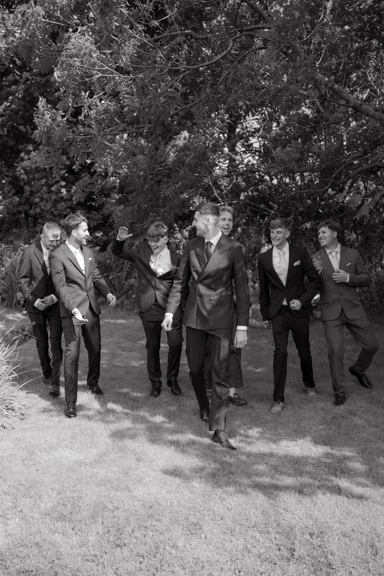 A group of formally dressed people walking and laughing together outdoors in a black and white photograph.