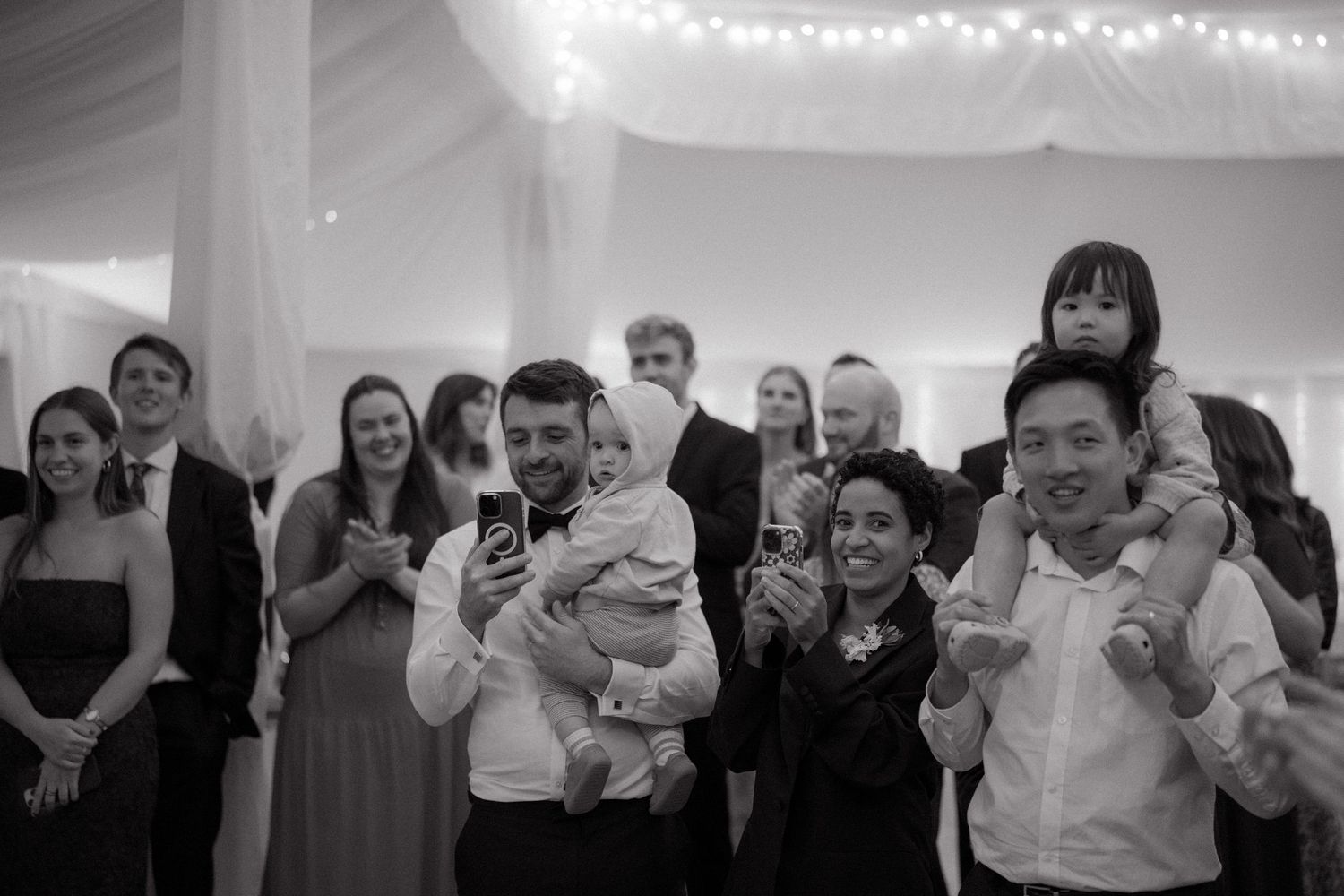 Black and white wedding reception photos show guests dancing and celebrating together under string lights.
