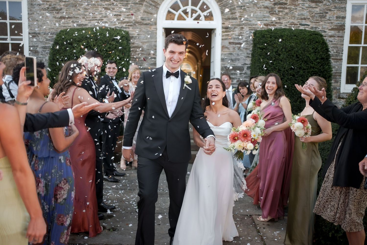 A couple shares their first dance at a rustic stone venue while wedding guests look on with phones raised to capture the moment.