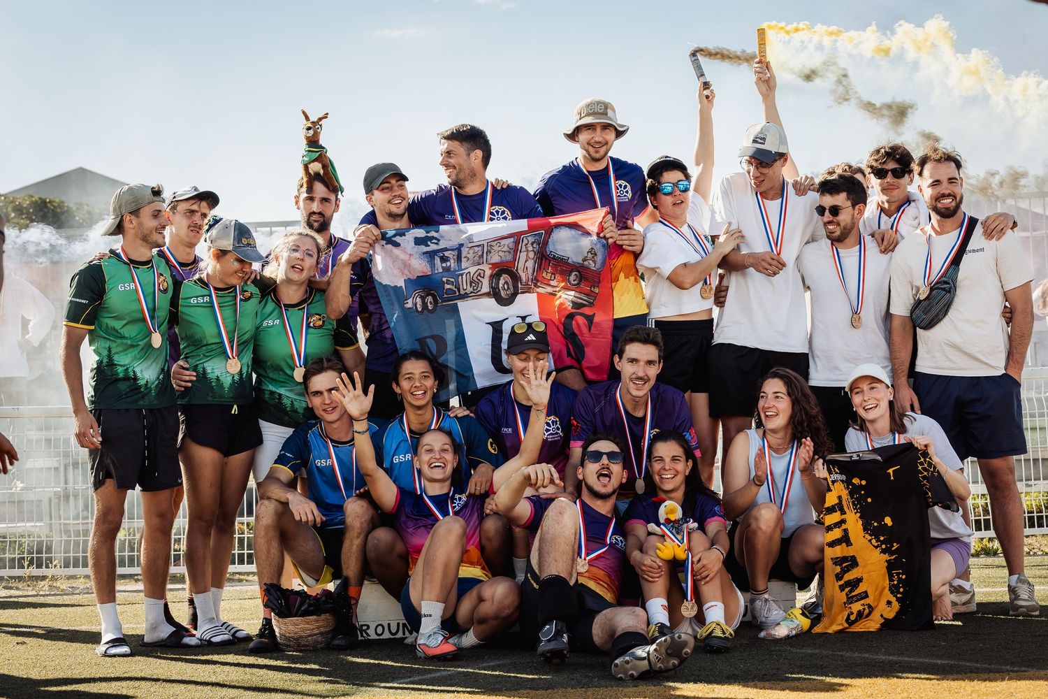 Large group of athletes posing together with medals and trophies celebrating a sports tournament victory outdoors.