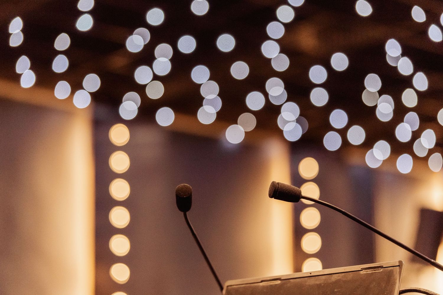 Elegant conference podium with two microphones and bokeh lights glowing in the background at a formal event.