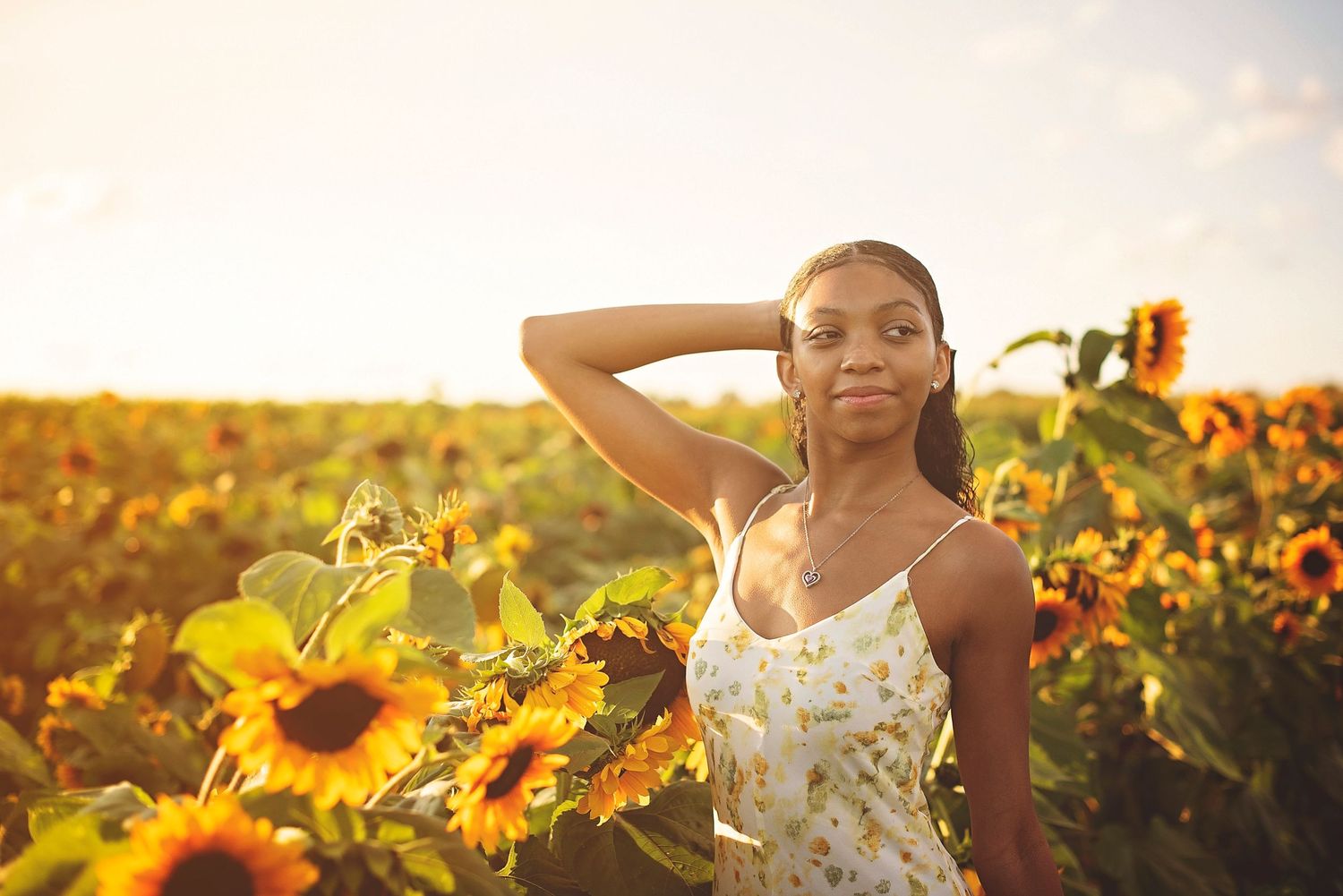 Figure poses elegantly among sunflowers during golden hour wearing a white summer dress.