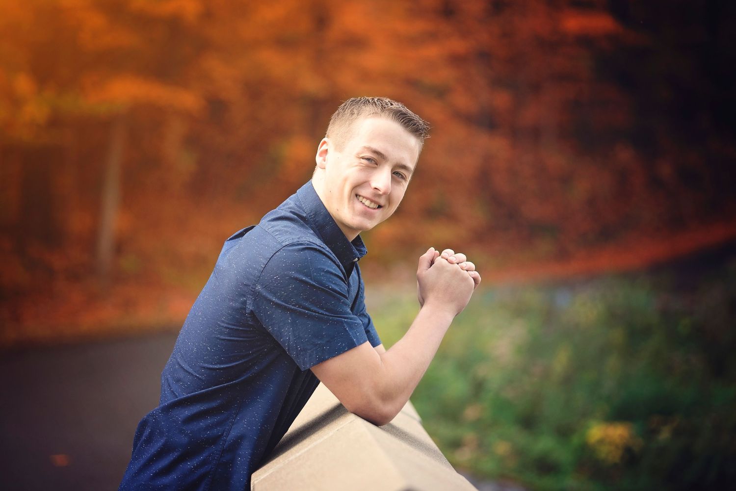 Person in navy polo shirt leaning on stone wall during autumn photoshoot.