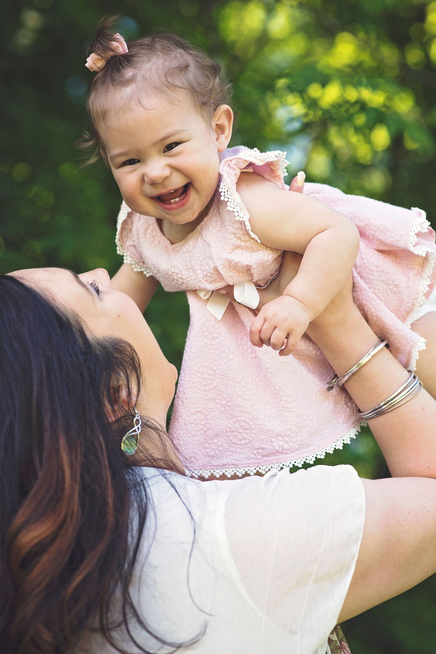 Joyful moment captured between parent and baby in pink dress outdoors.