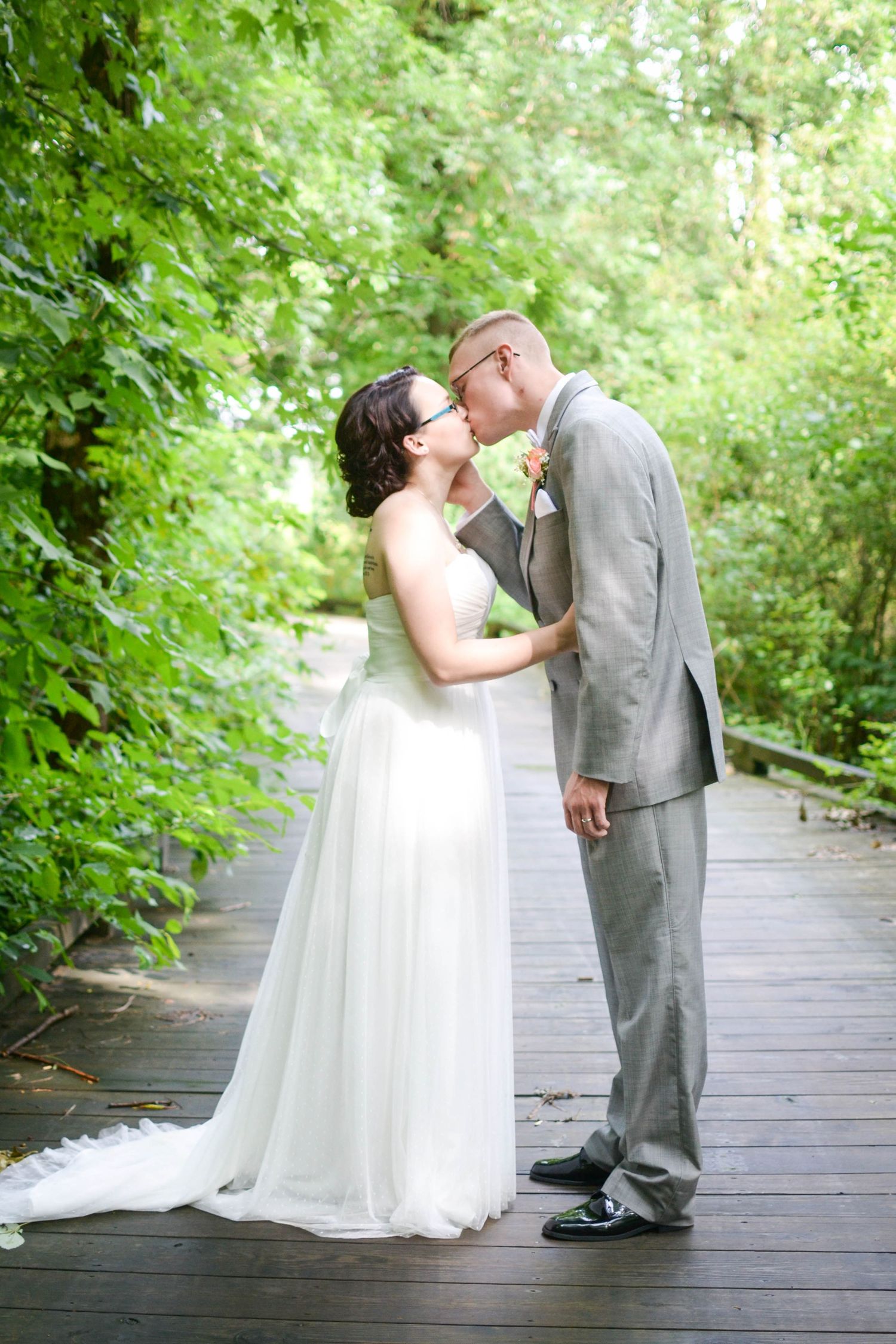 Bride and groom share romantic kiss on wooden boardwalk surrounded by lush greenery.