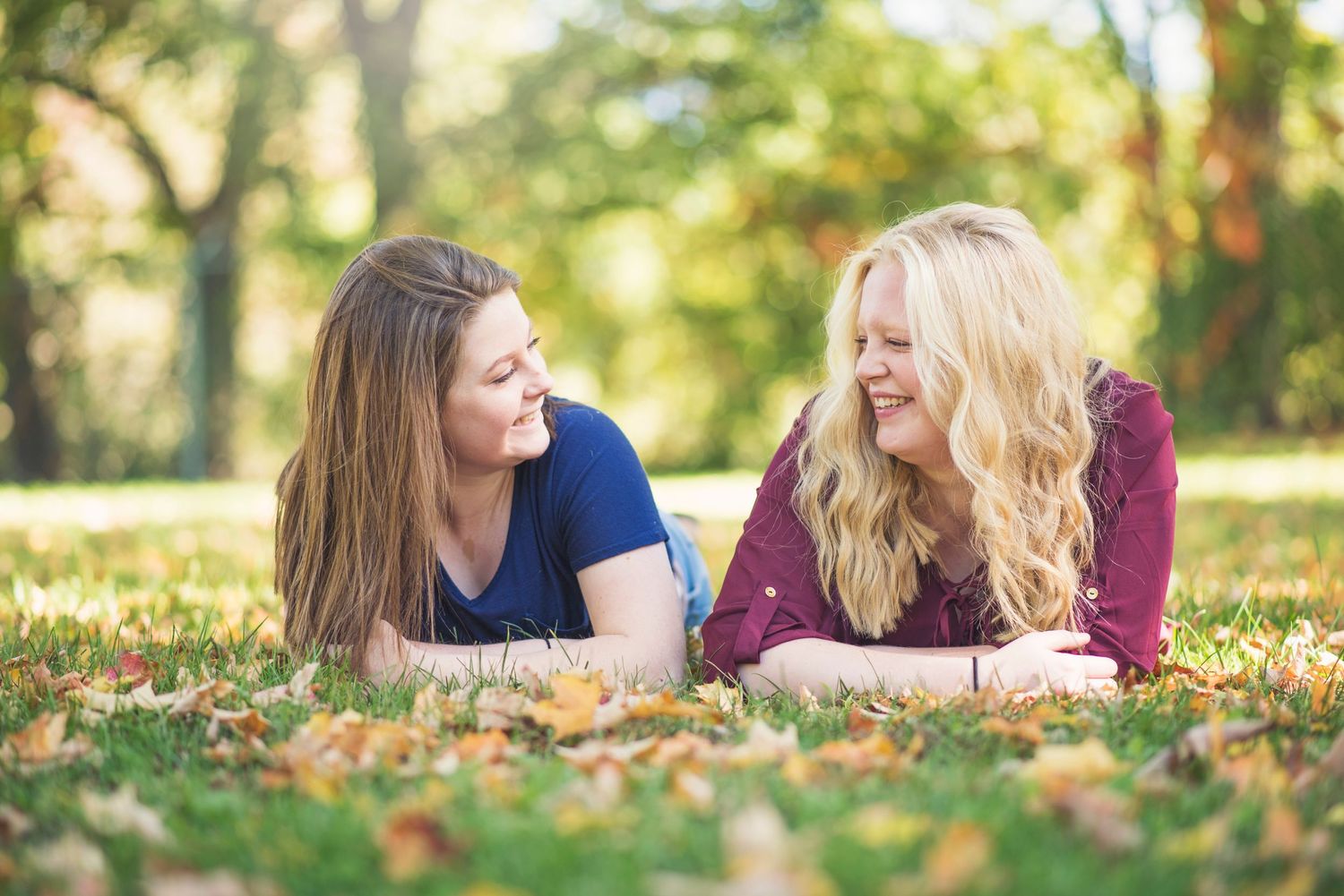 Two people lying on fallen autumn leaves having a conversation outdoors.