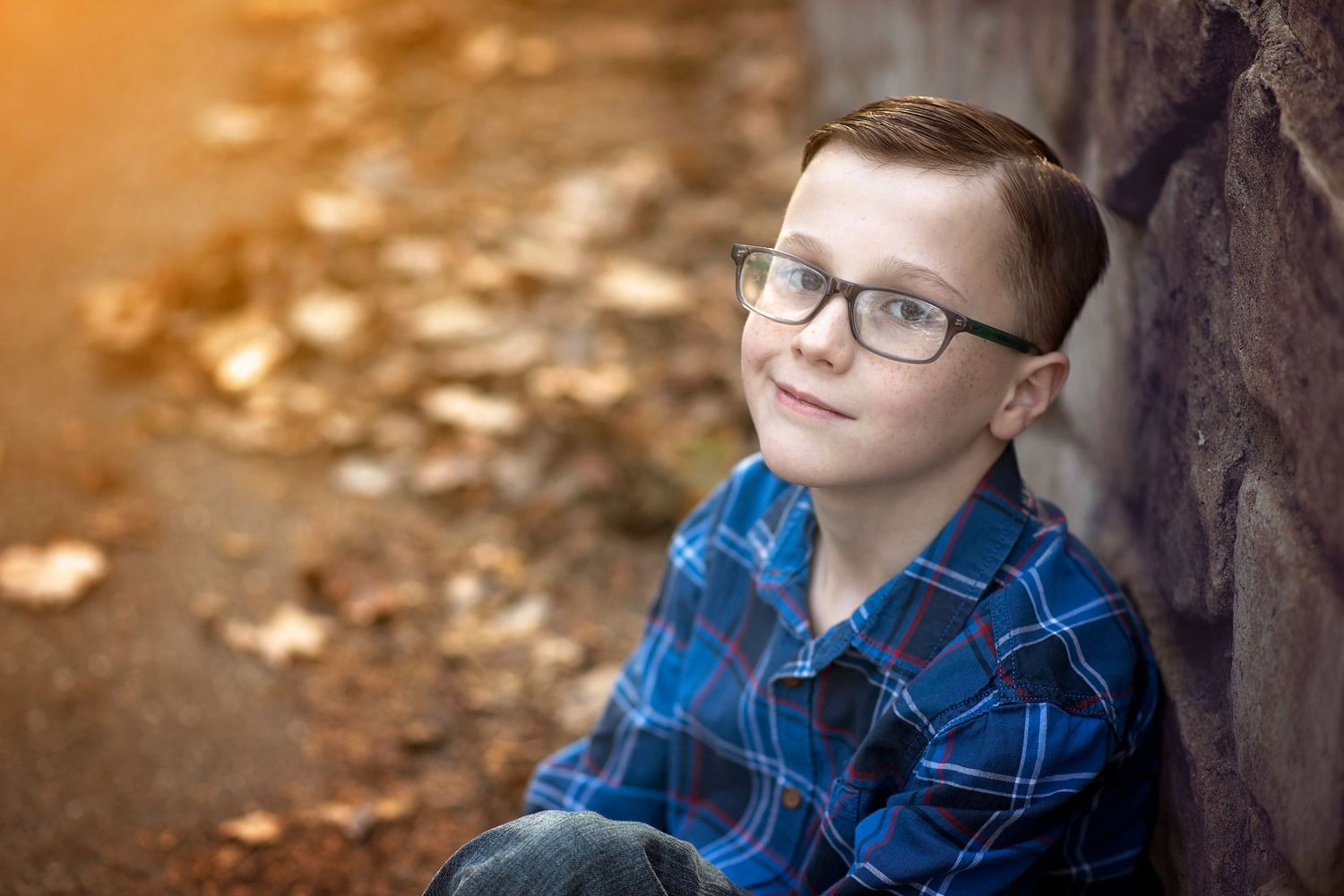 Portrait in autumn with glasses and plaid blue shirt against fallen leaves in warm lighting.