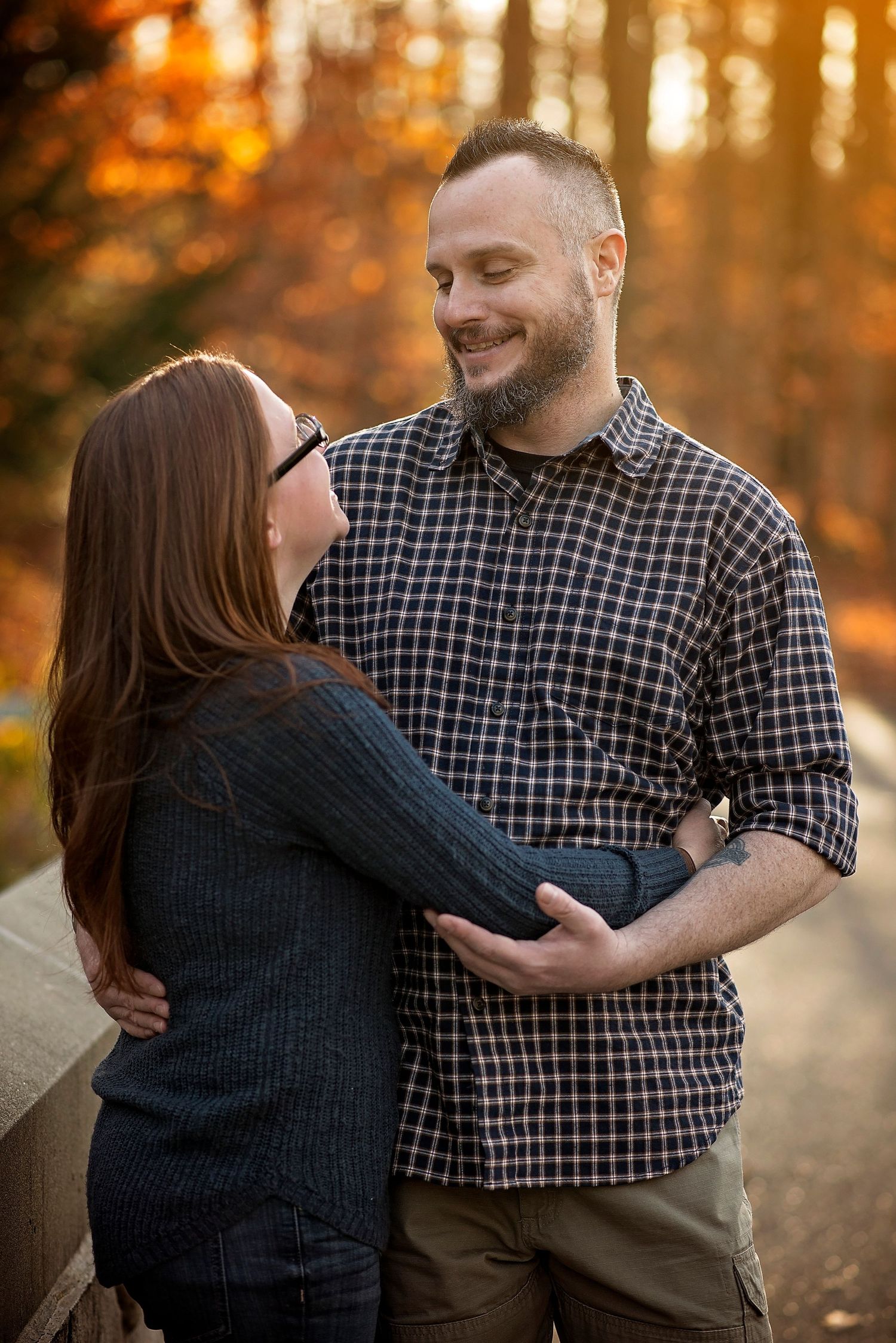 Couple embracing in autumn forest with warm sunset lighting filtering through trees.