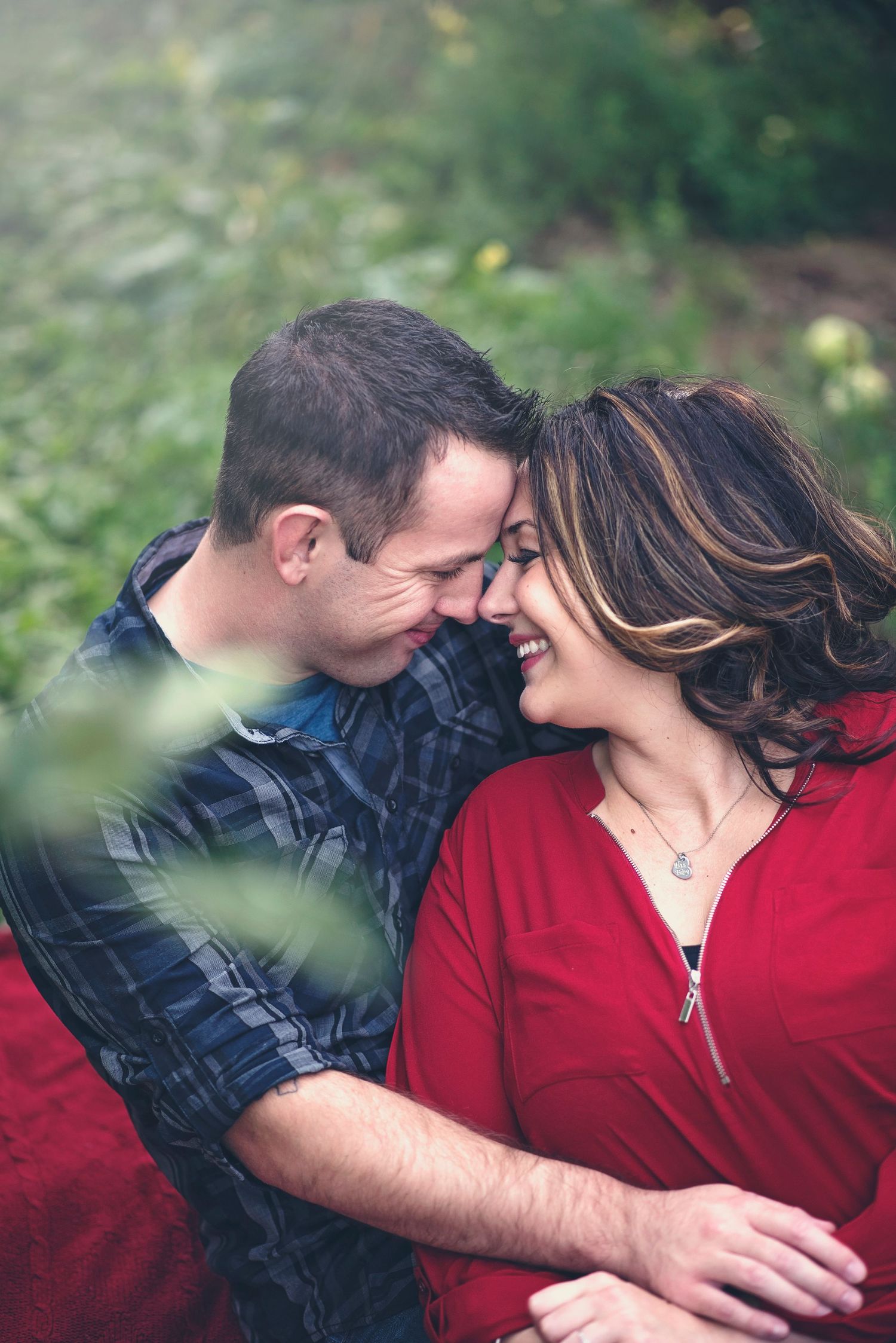 Intimate moment between couple in red and plaid shirt among green leaves.