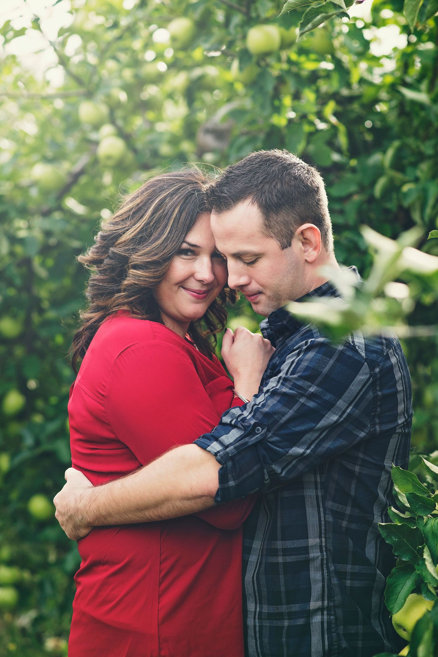 Intimate couple portrait in red and plaid among green foliage.