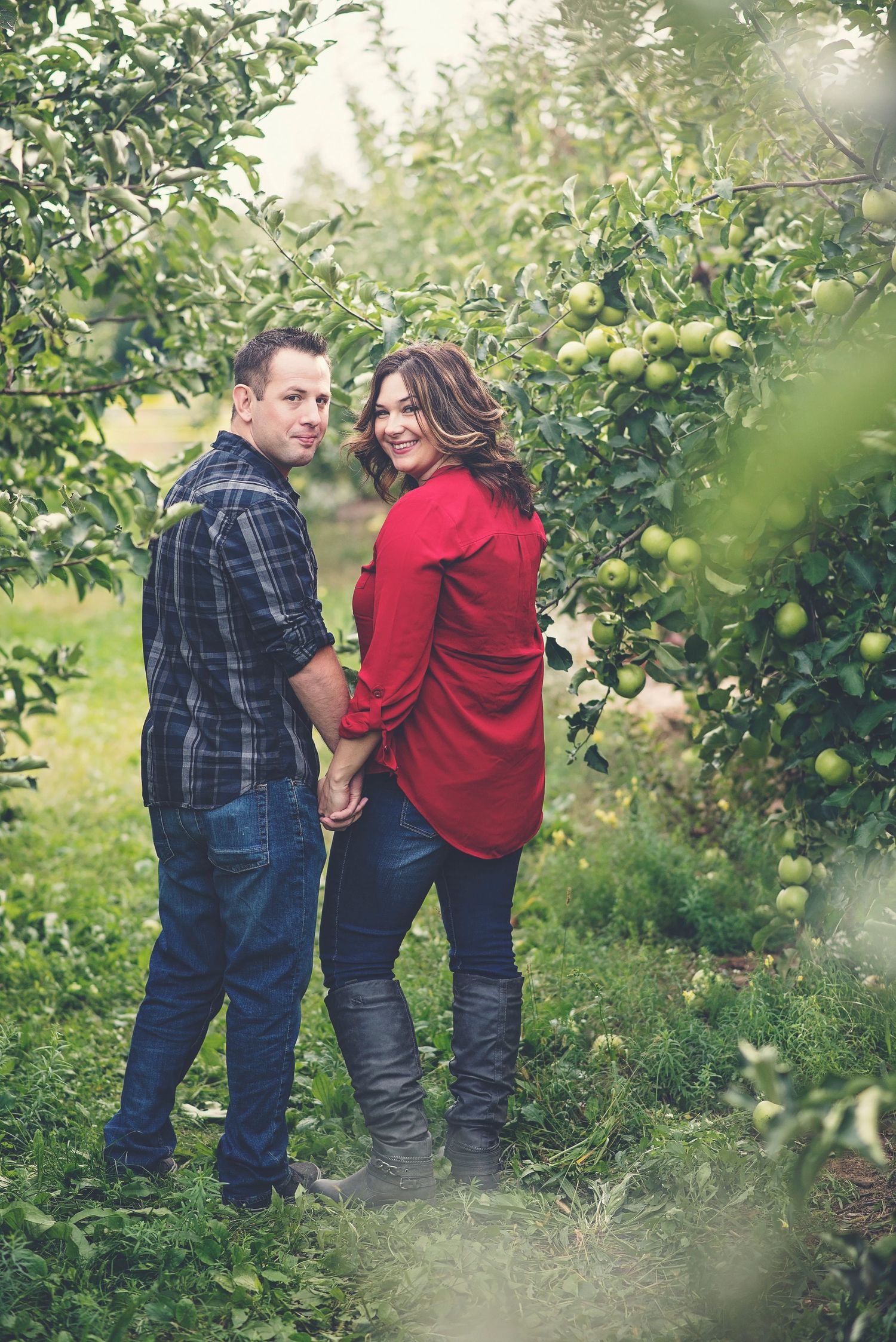 Couple holding hands in apple orchard looking back at camera.