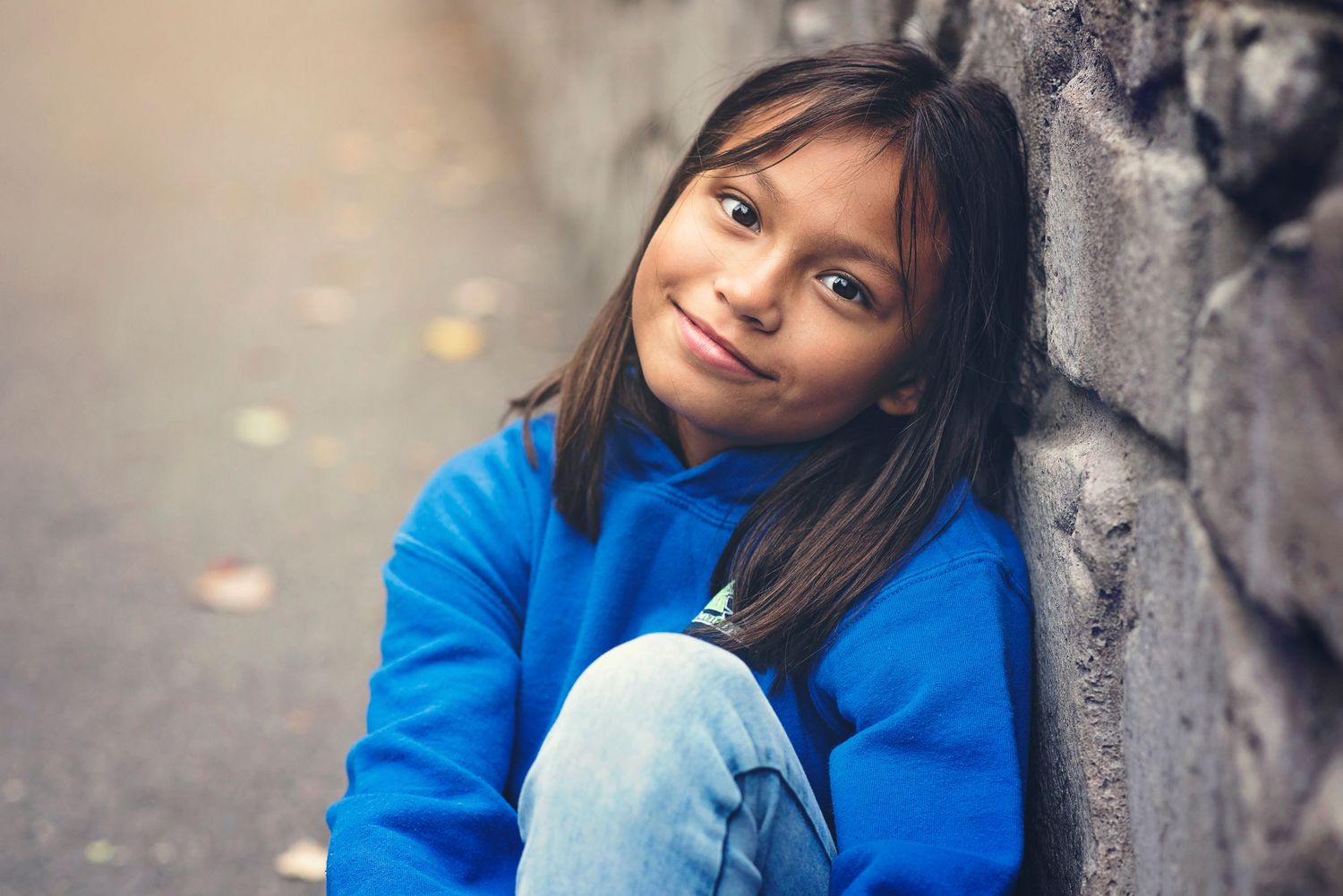 Person in bright blue sweater sits casually against stone wall during autumn.