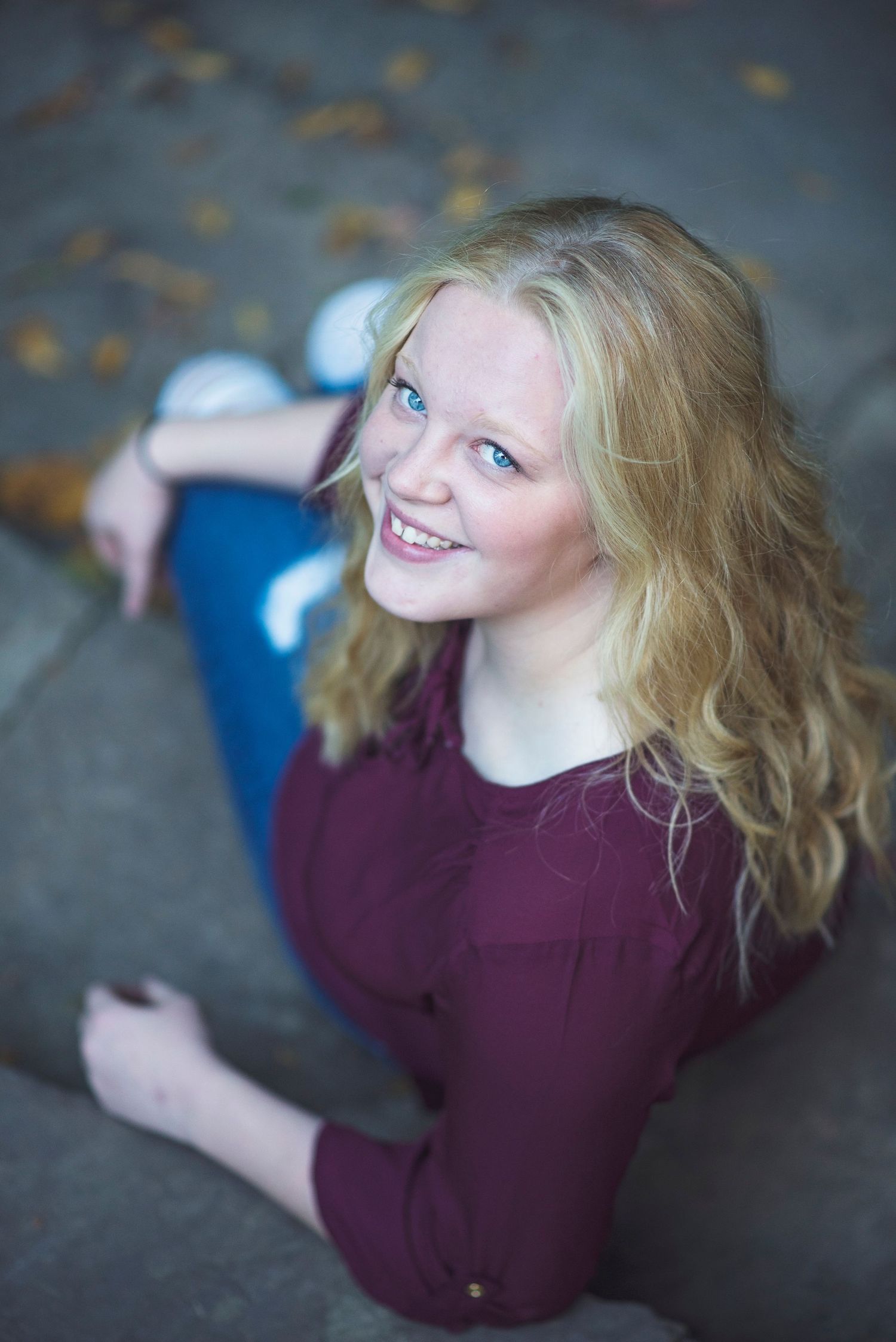 Person in burgundy top sitting outdoors with long blonde hair on an autumn day.