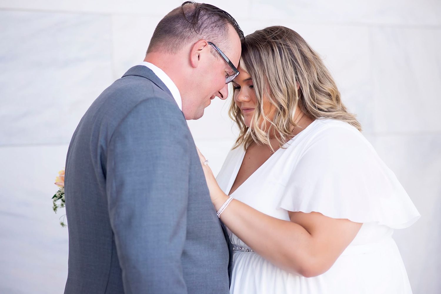 Intimate wedding portrait of a couple in gray suit and white dress sharing a tender moment.