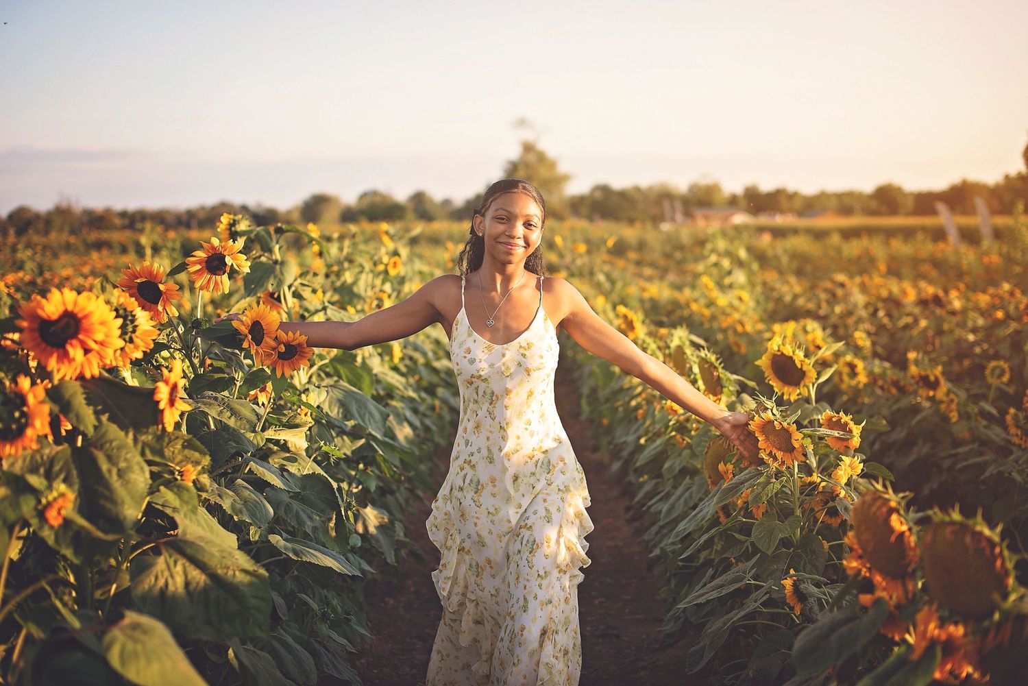 Figure in a flowing white dress twirls joyfully among tall sunflowers during golden hour.