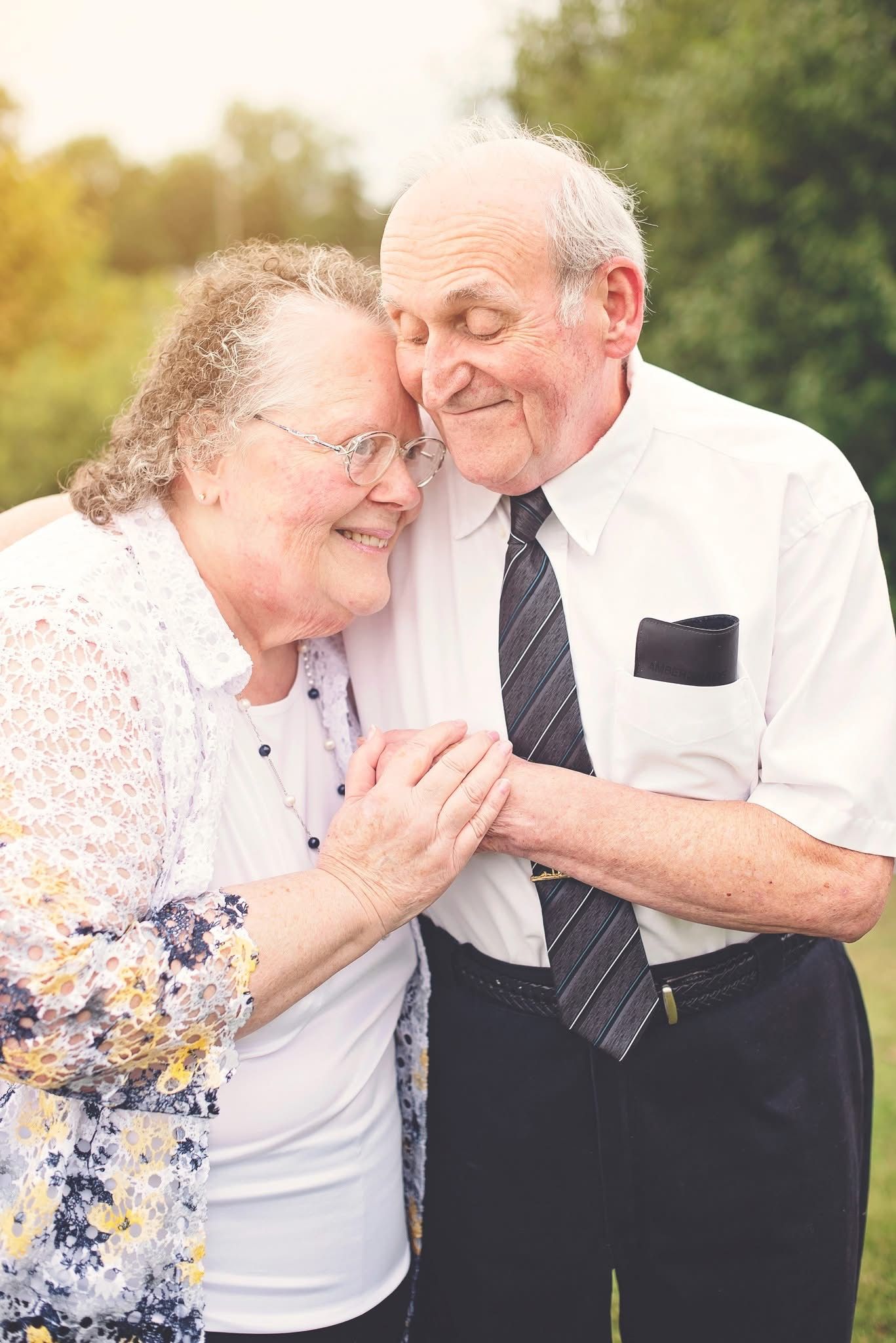 Candid portrait of an elderly couple laughing and embracing outdoors in formal attire.