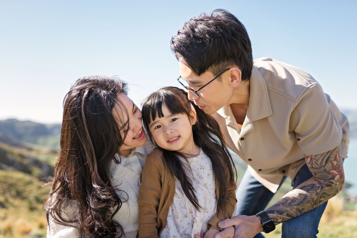 A happy family shares a tender moment together outdoors against a scenic mountain backdrop on a sunny day.
