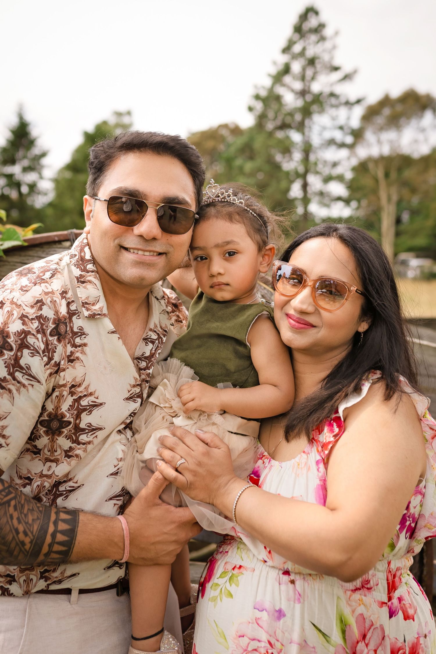 A family poses together outdoors with trees in the background on a sunny day.