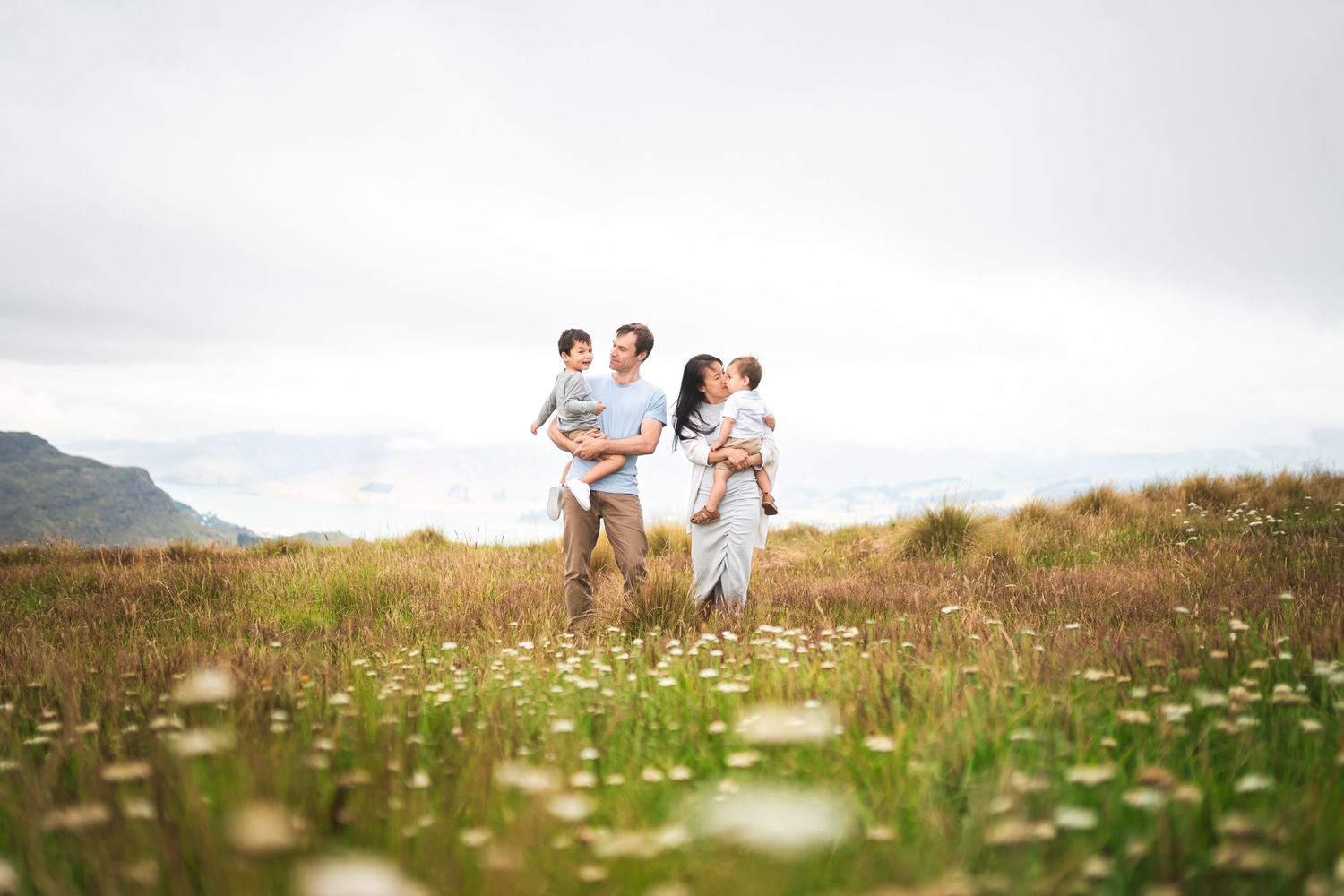 Family members running together through a mountain meadow dotted with white flowers.