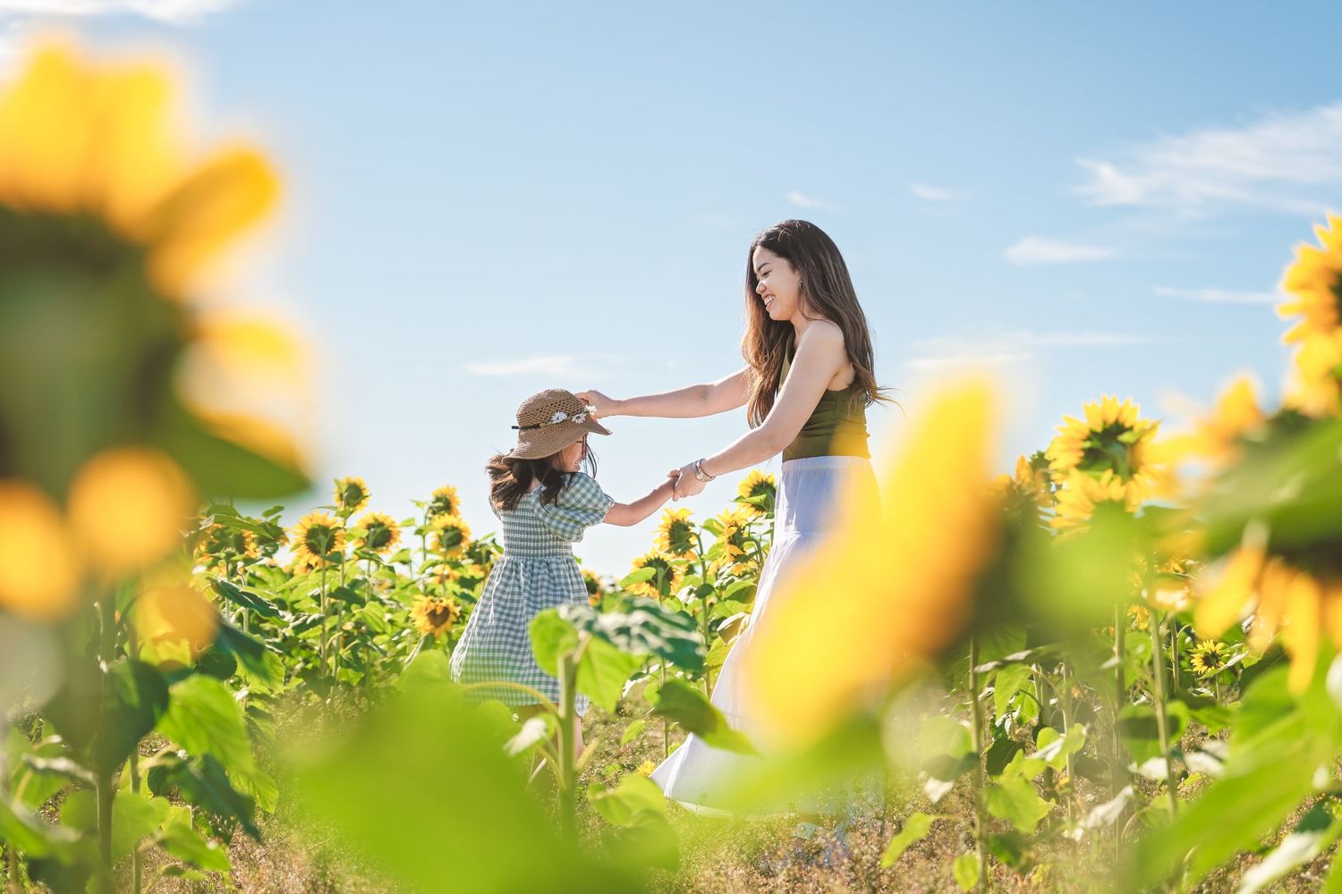 Mother and daughter dancing together in sunlit sunflower field.