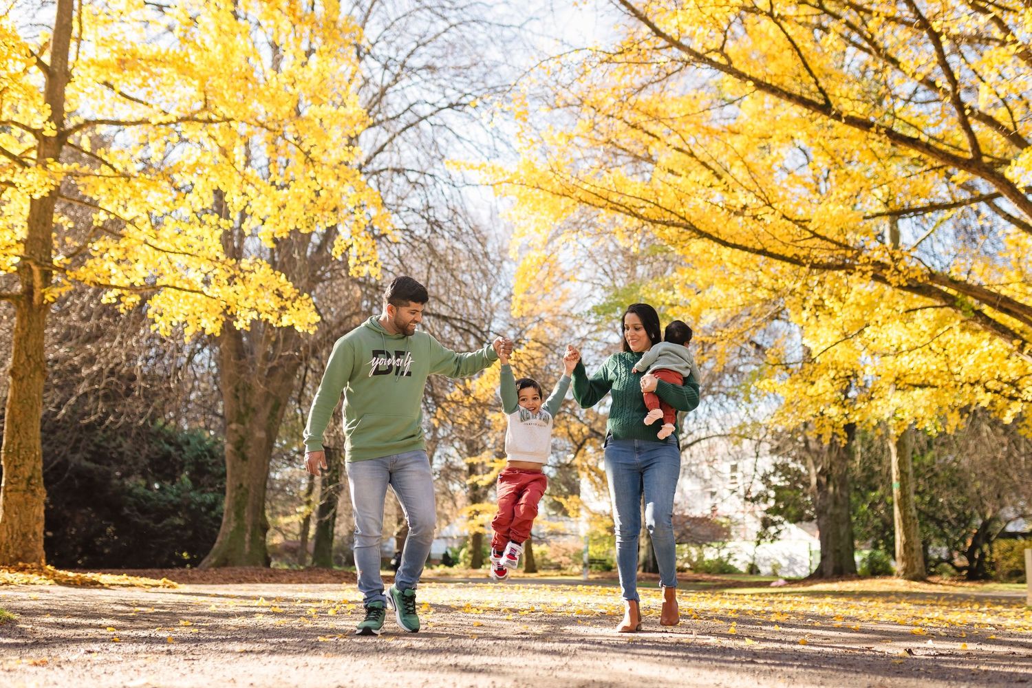 A group of people walk beneath vibrant yellow autumn trees on a path in a park during fall season.