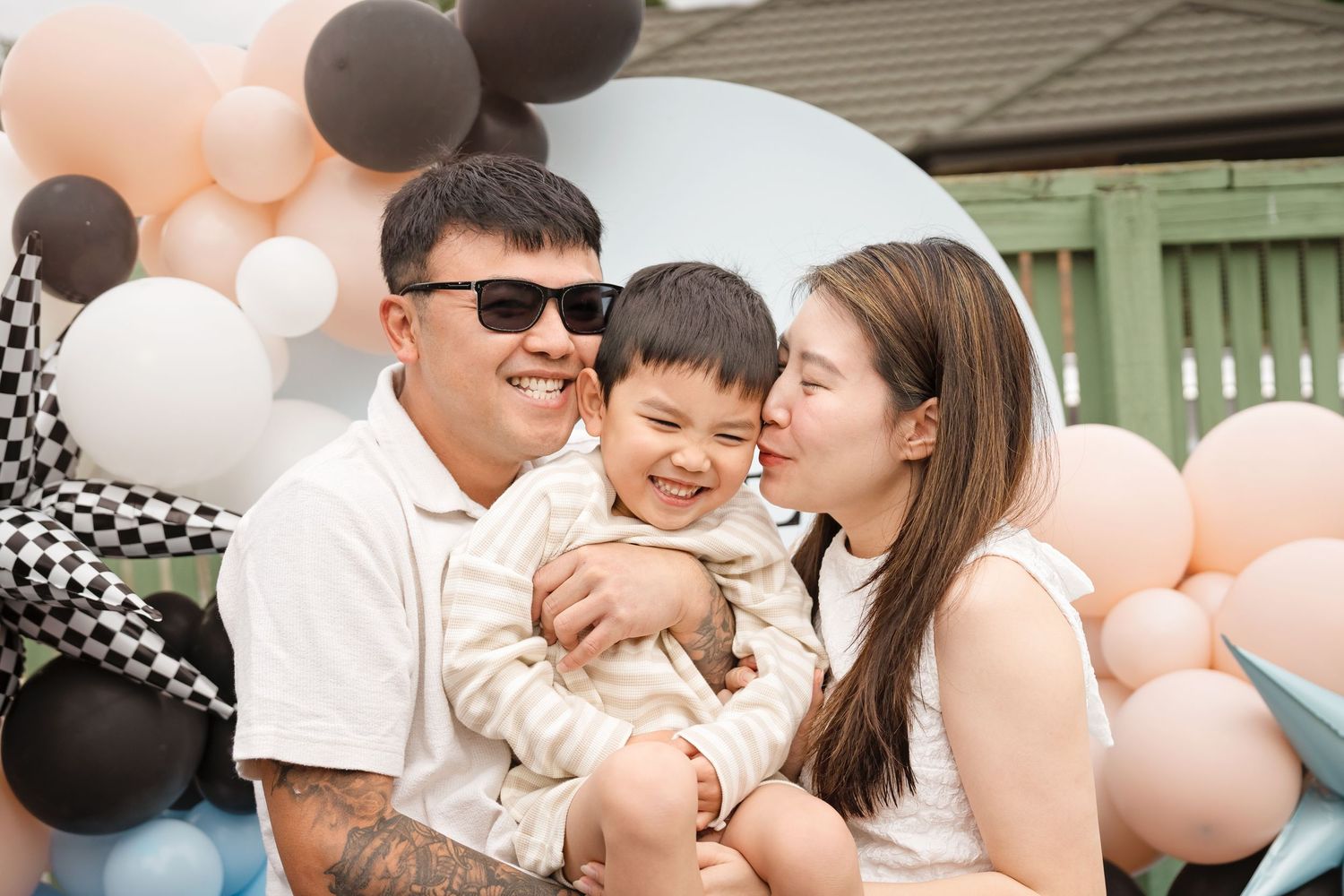 Happy family with parents and young son celebrating a birthday party with colorful balloons backdrop.