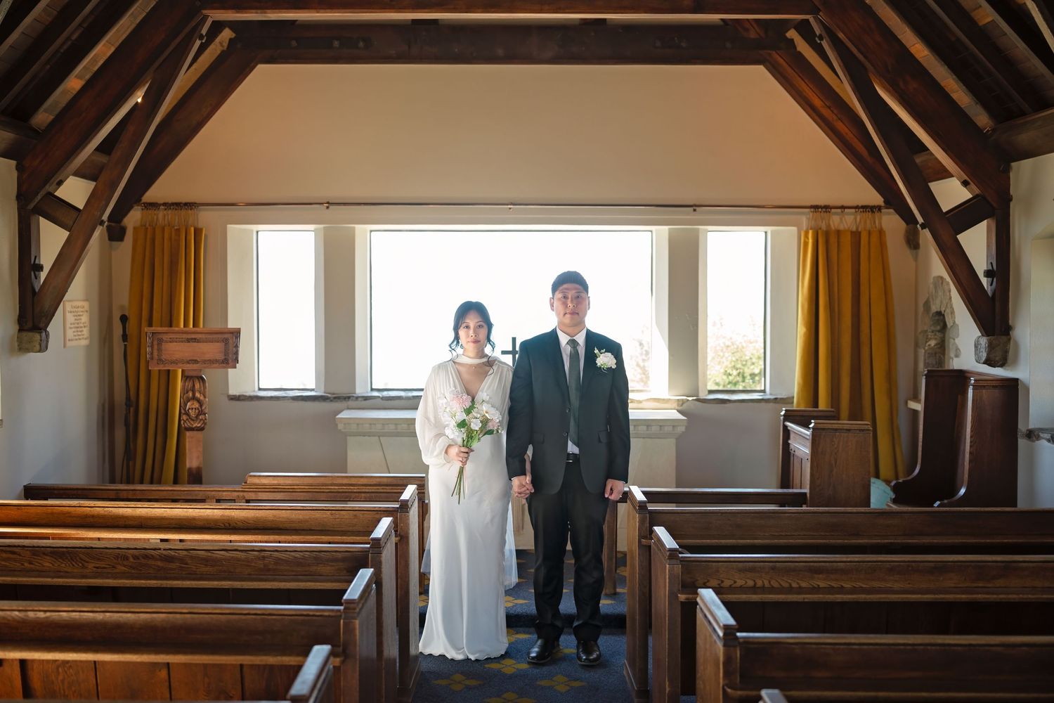 Bride and groom stand together in a charming wooden chapel interior on their wedding day.