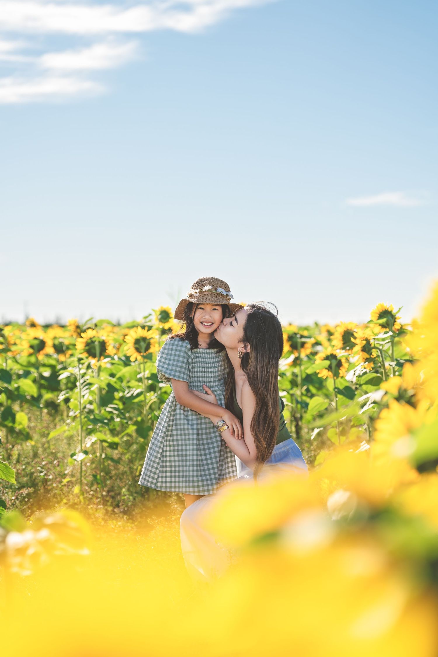 Mother and daughter sharing a tender moment in a sunflower field on a sunny day.