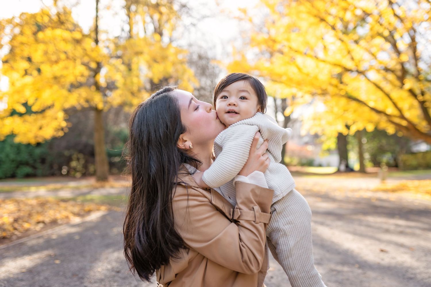 A tender moment shared between parent and child outdoors during autumn with golden yellow trees in the background.