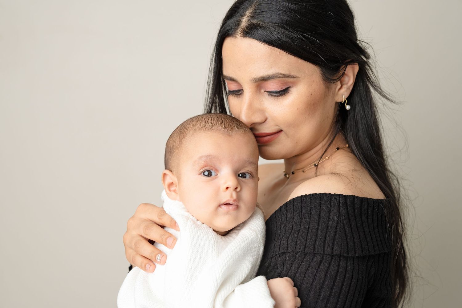 A tender moment between parent and baby, with soft lighting against a neutral background.