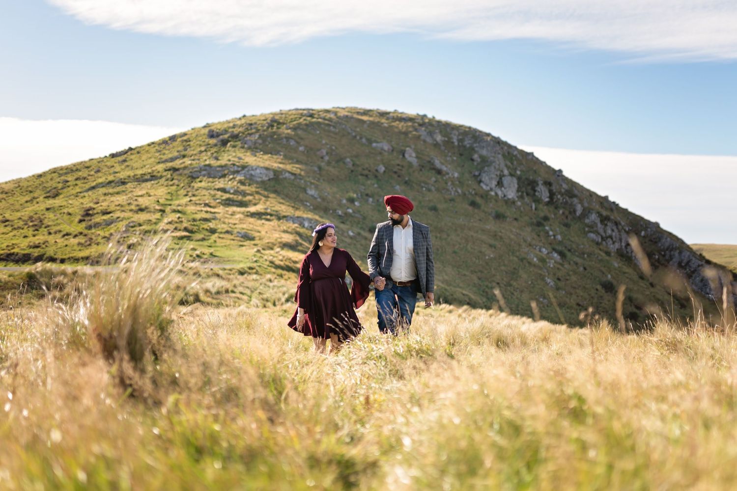 Couple walking together on a scenic mountain trail with golden grass and blue sky on a sunny day.