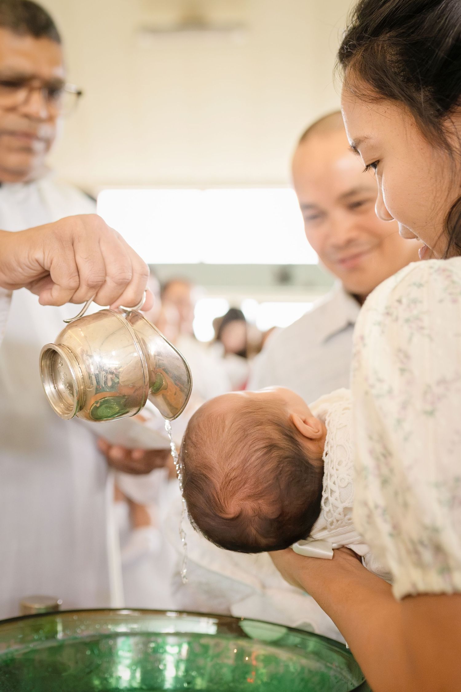 Priest pouring holy water over infant's head during Catholic baptism ceremony held in a church.