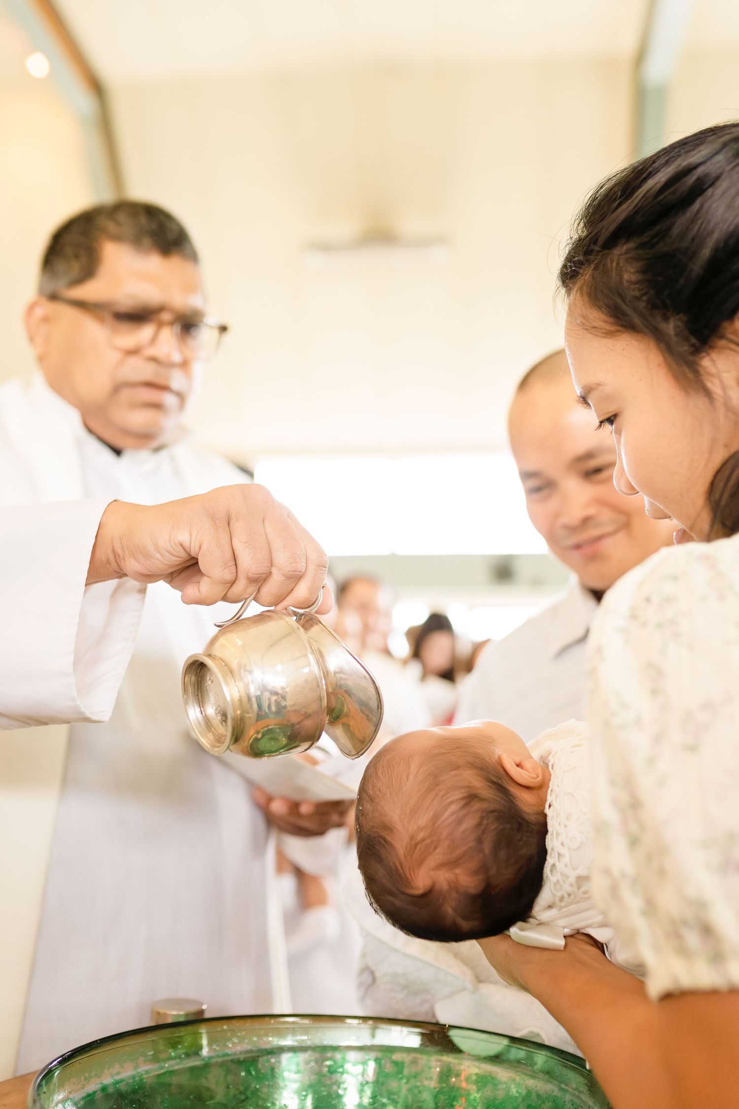 Catholic priest pouring holy water over newborn baby during baptism ceremony at church.