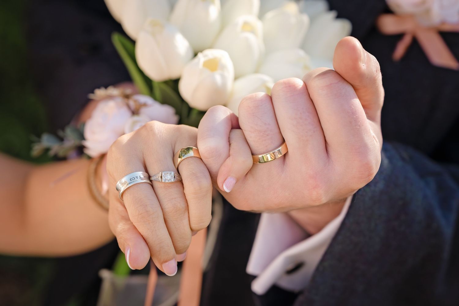 Newlywed couple holding hands showing wedding rings with white tulip bouquet in background.
