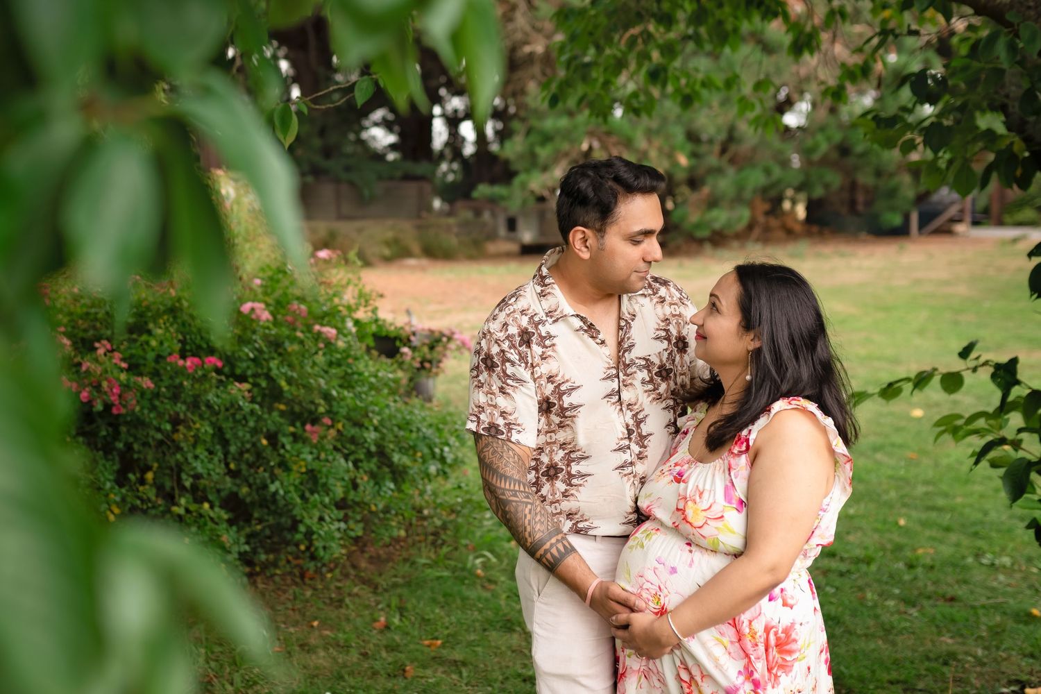 A couple in floral outfits share a tender moment together in a lush garden setting during a photo session.