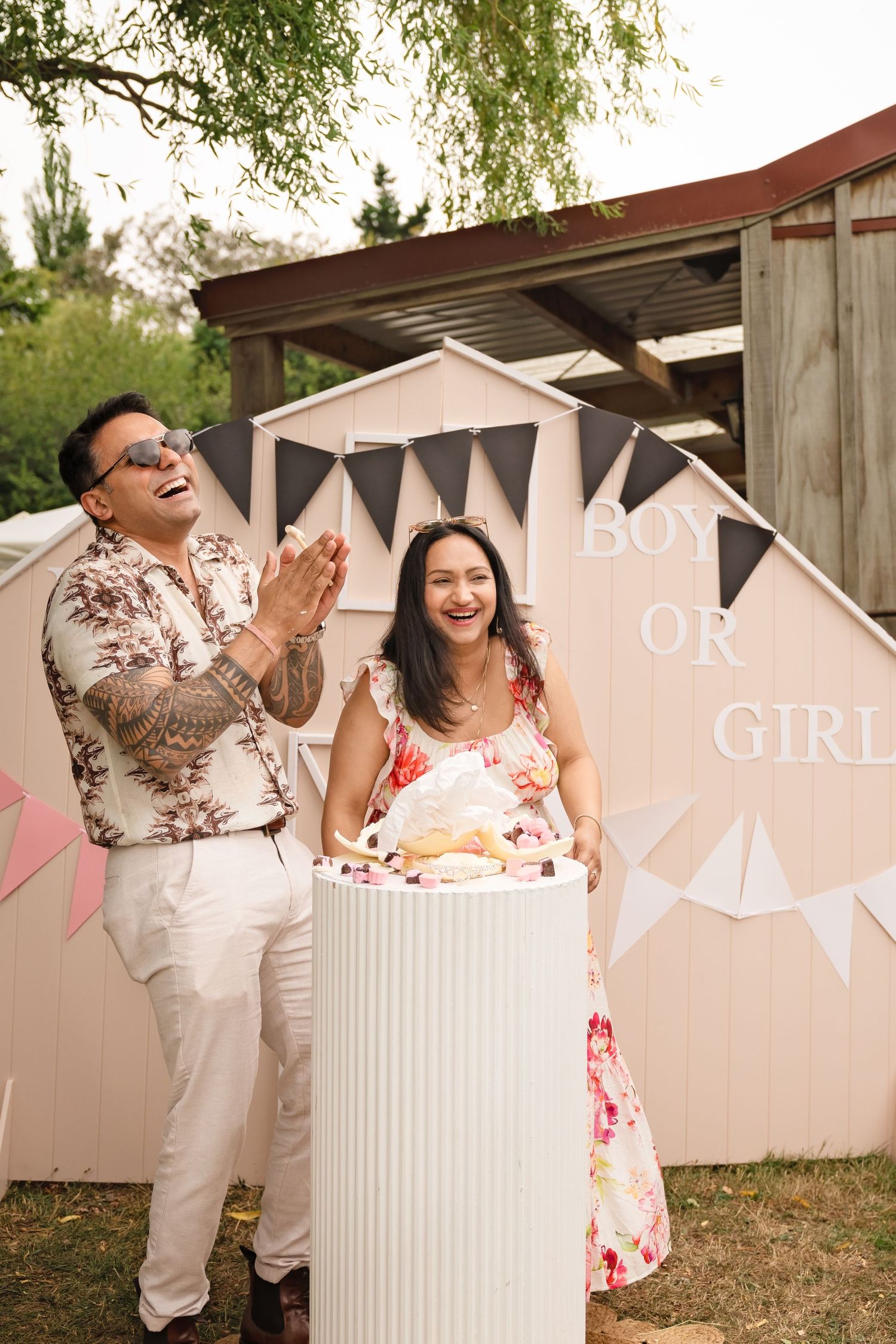 Gender reveal party decorations with pink and blue banners and balloons set up in an outdoor garden setting.