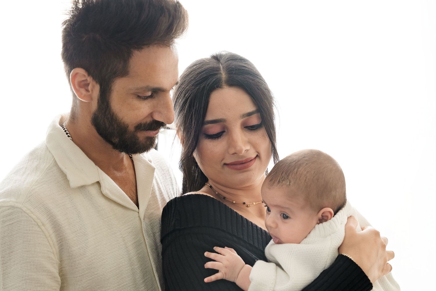 A loving family embraces their baby in a tender moment during a minimalist studio photo session.
