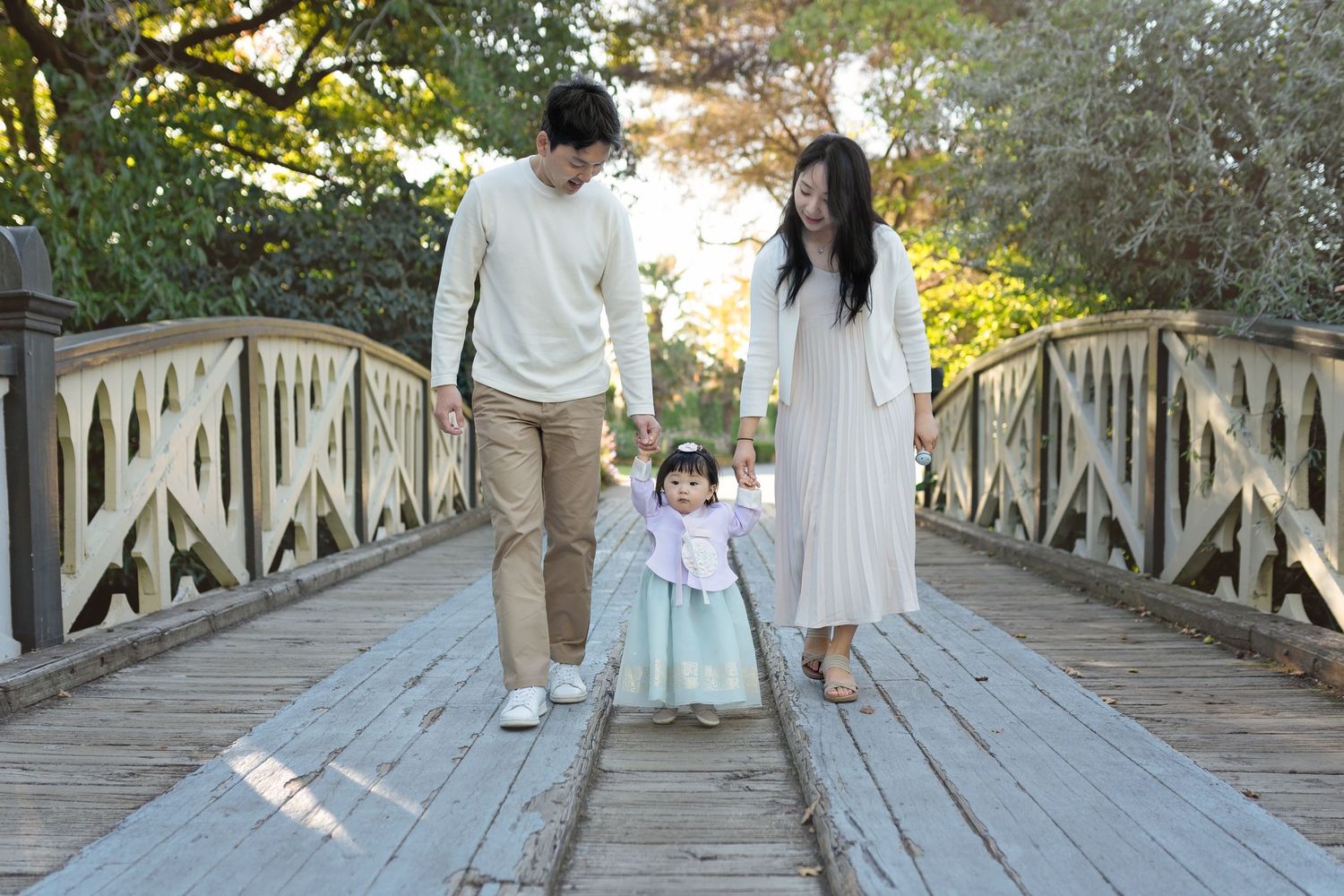Family walking together on wooden bridge surrounded by autumn trees.