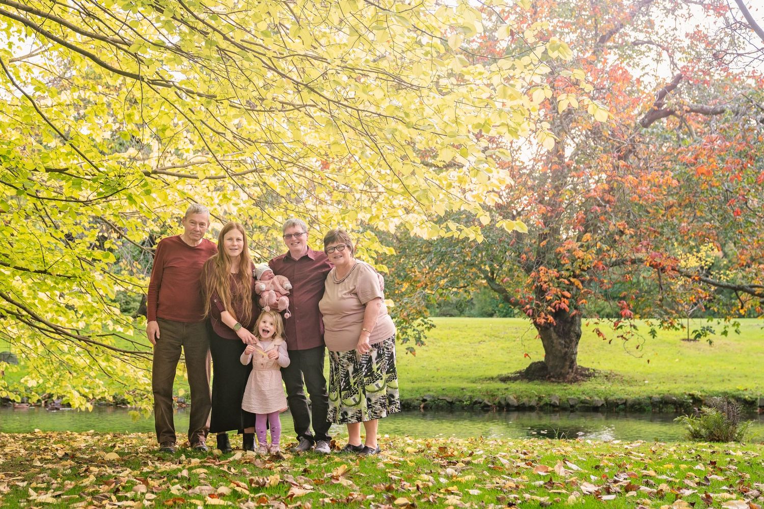 Family group poses beneath vibrant yellow autumn trees in a park during a fall photo session.