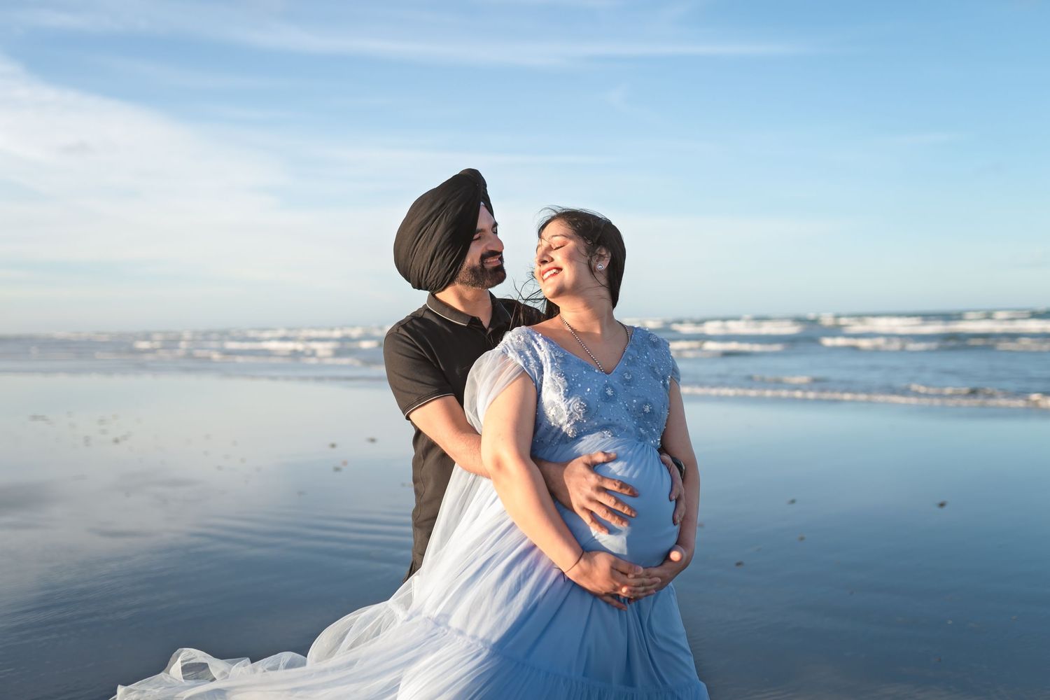 Romantic beachside maternity photo with waves crashing in the background.