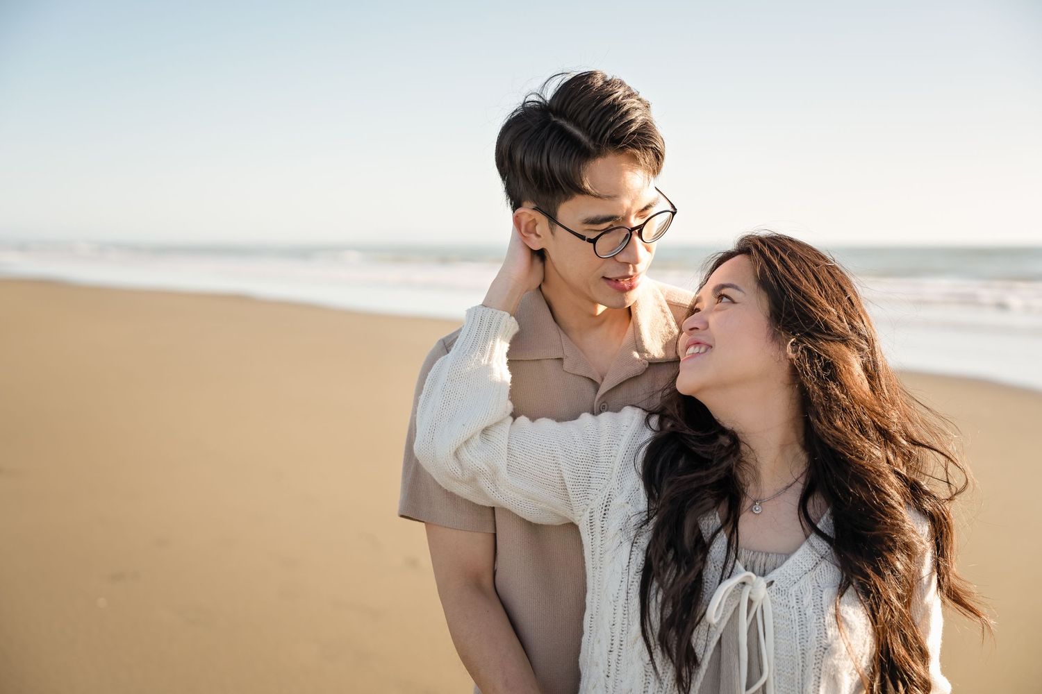 Romantic couple sharing a tender moment on a sunny beach, with ocean waves in the background.