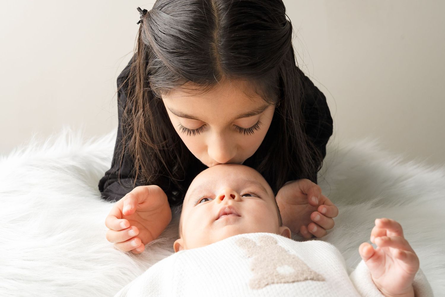 A tender moment captured between caregiver and baby lying on soft white bedding.