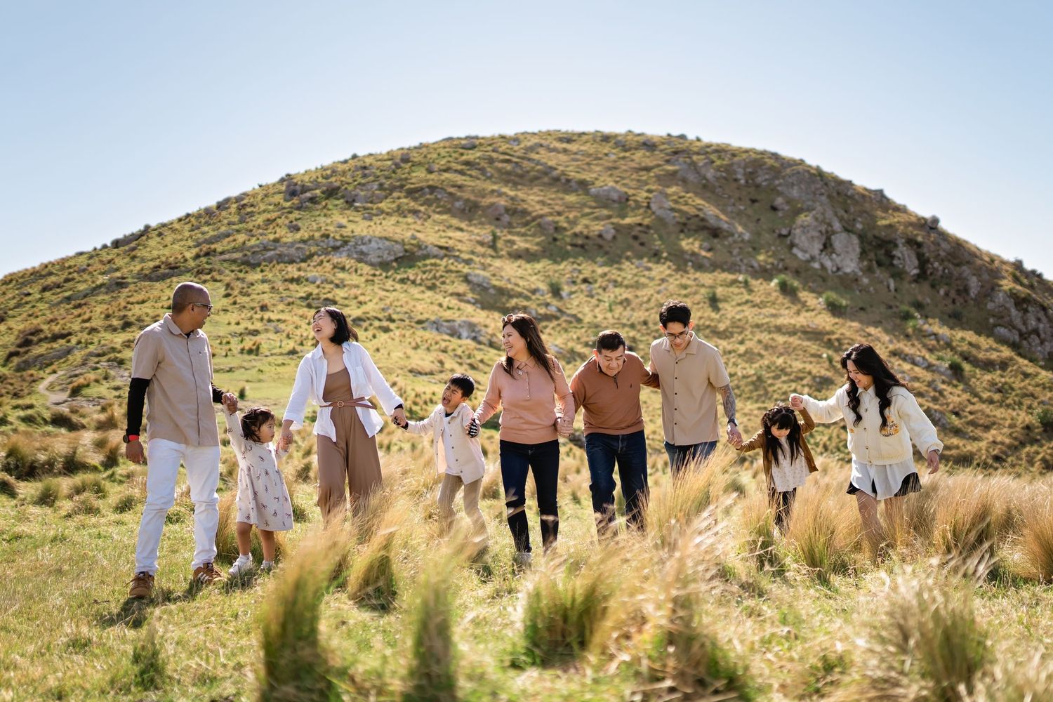 A group walks together through golden grass fields with mountains in the background on a sunny day.
