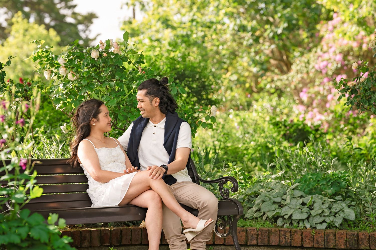 Romantic couple sitting on a bench in a green garden, holding hands and smiling.