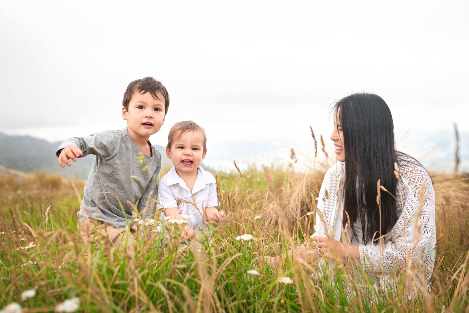 Mother and children playing together in tall grass on a hillside.