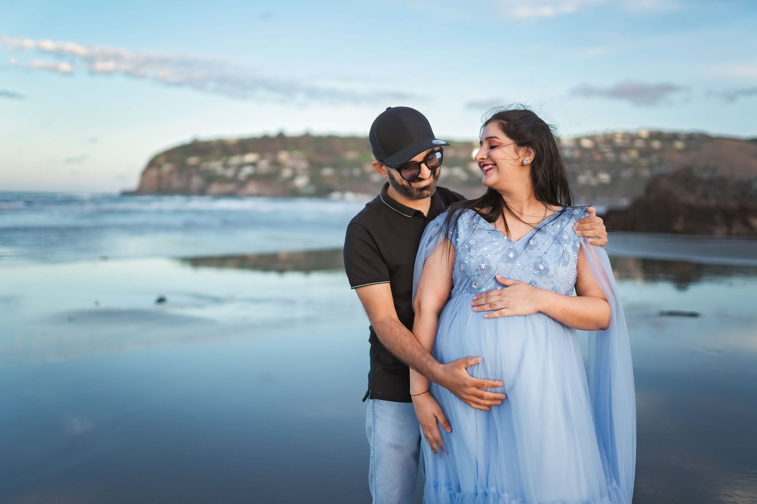 Couple sharing a tender moment during beach maternity photoshoot at sunset.