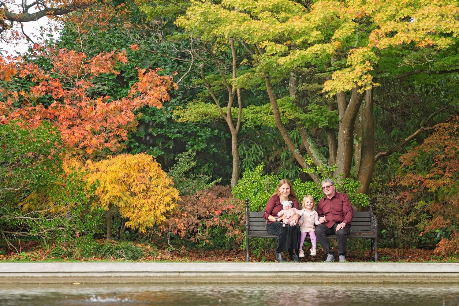 Colorful autumn trees line a park path where people enjoy a peaceful fall day on wooden benches.